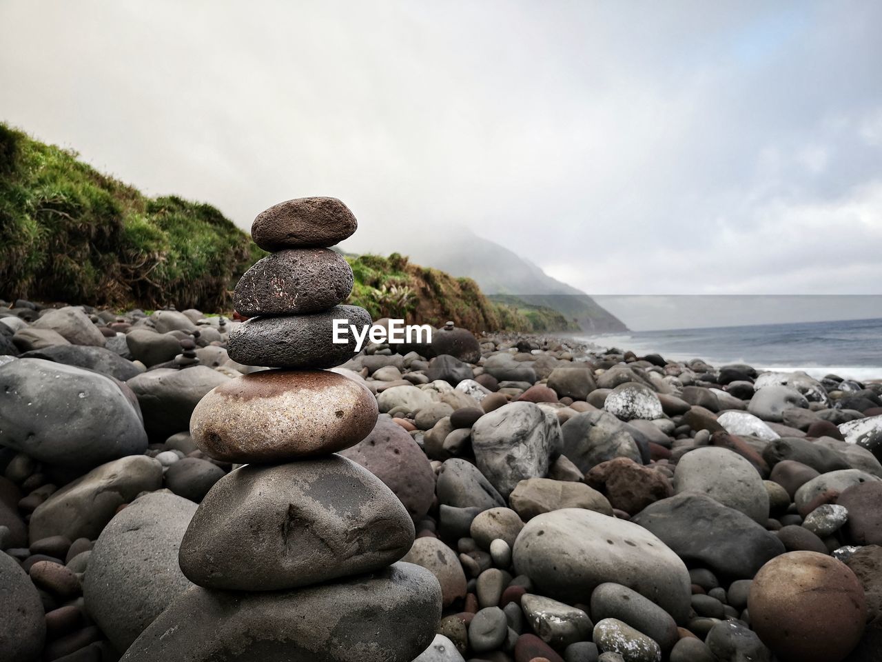 rock, water, land, shore, sky, sea, beach, nature, pebble, stone, coast, cloud, beauty in nature, tranquility, scenics - nature, tranquil scene, boulder, ocean, environment, no people, zen-like, balance, outdoors, body of water, day, coastline, landscape, overcast, non-urban scene, idyllic, travel destinations, water's edge, horizon over water, travel, horizon