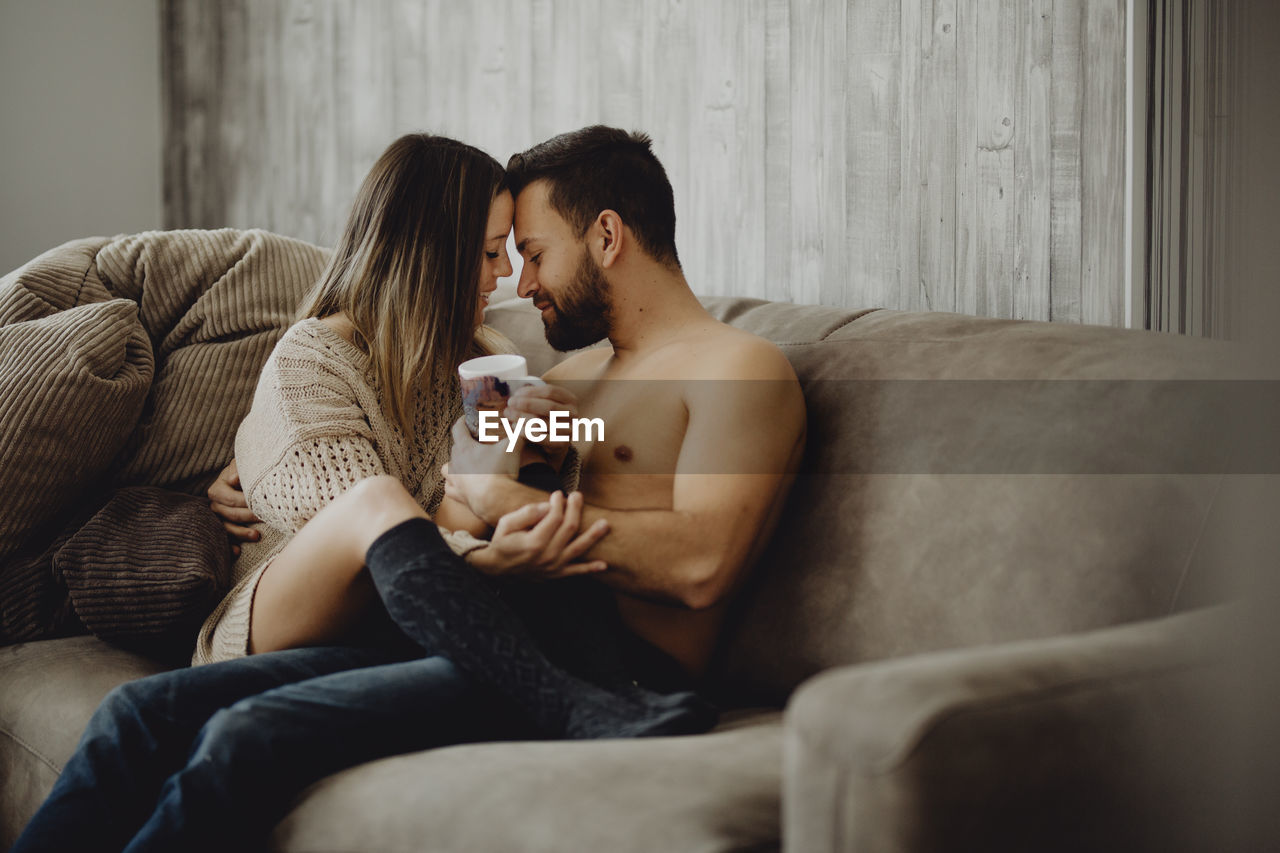 Happy man and woman with mug of hot beverage smiling and looking at each other while spending time at home in morning