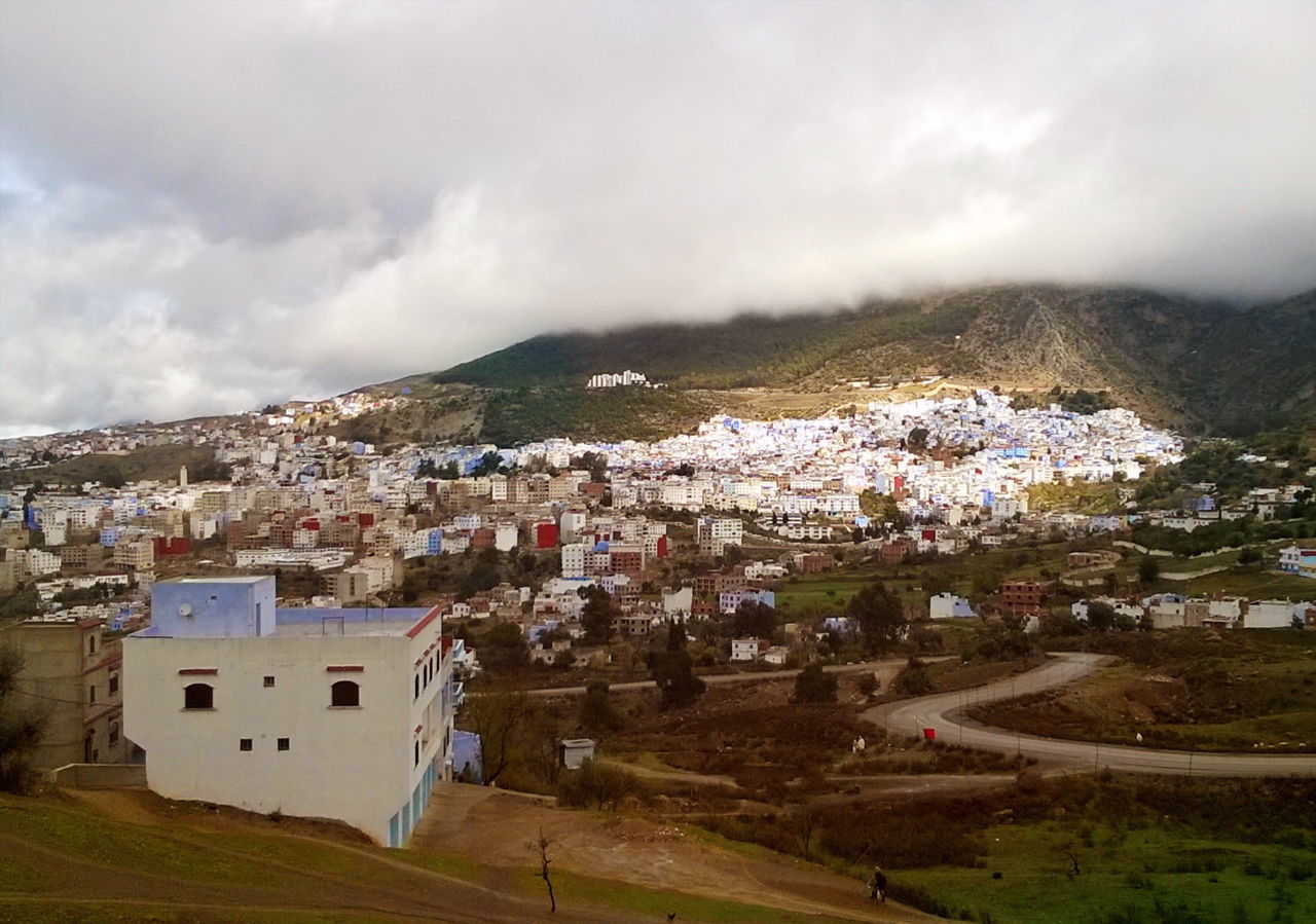 Townscape by mountain against cloudy sky