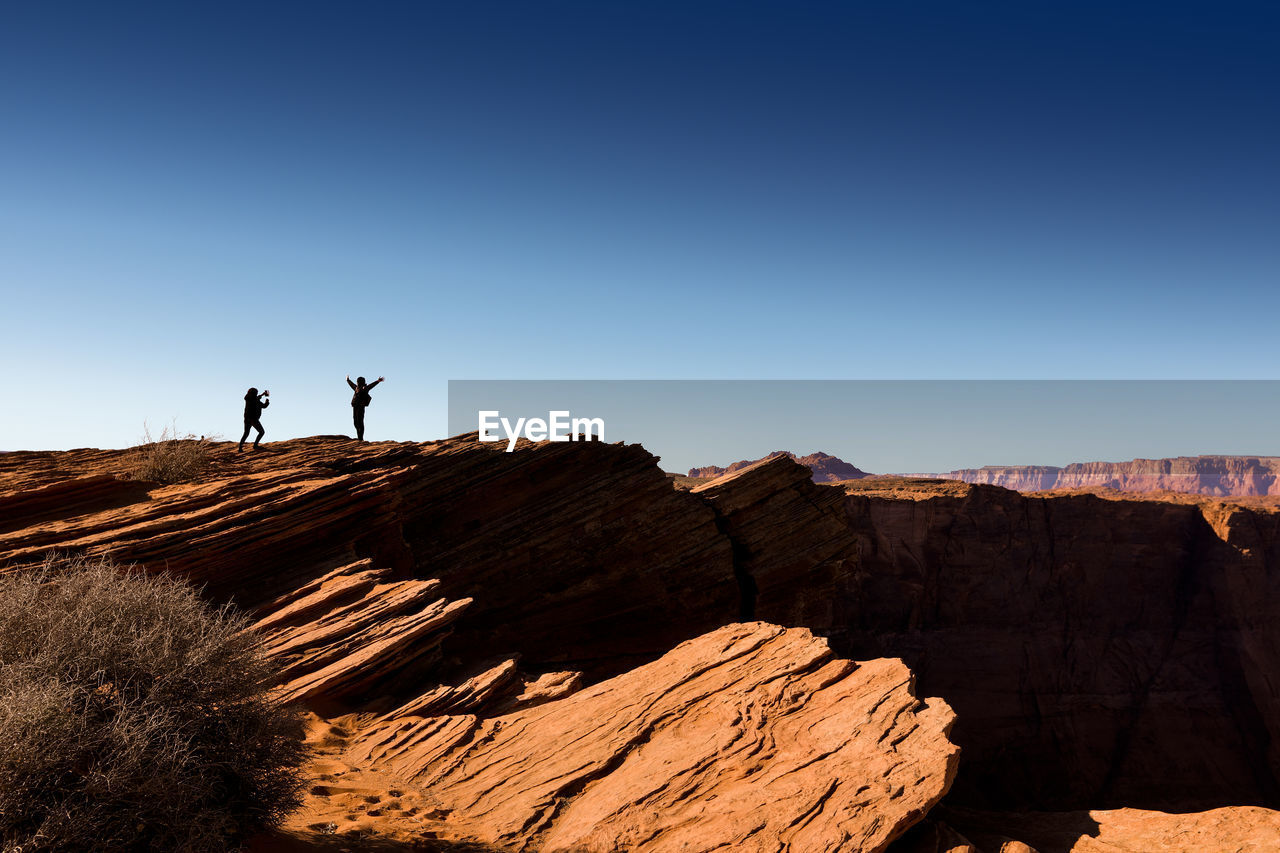 Low angle view of people standing on desert against clear blue sky