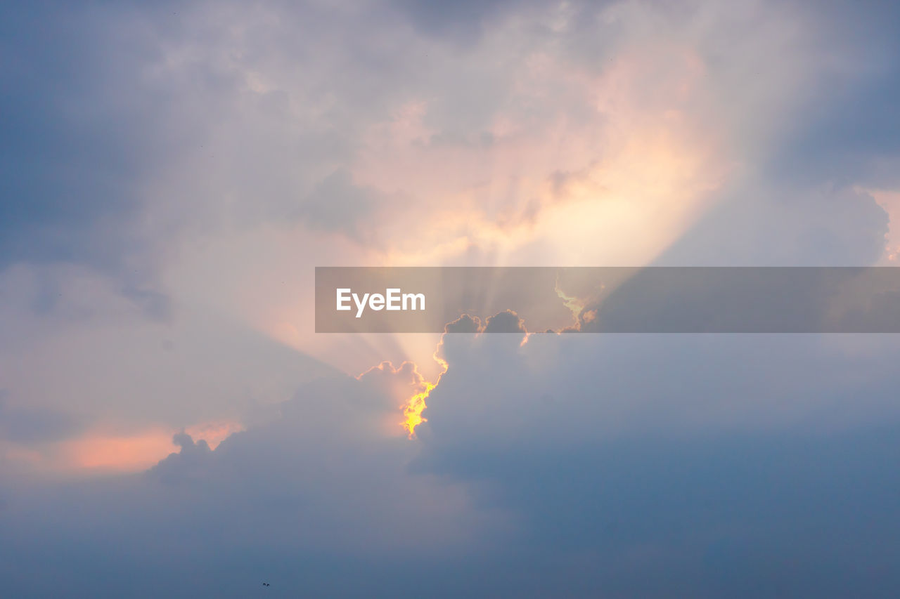 Low angle view of sunlight streaming through clouds during sunset