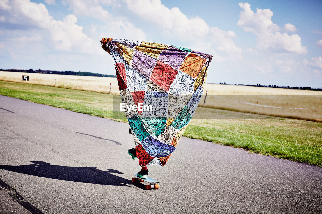 Low section of person holding colorful shawl while skating on airport runway