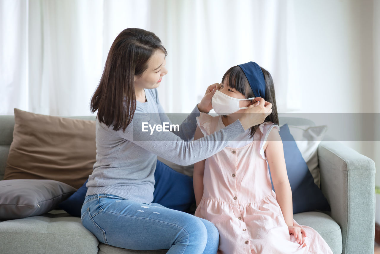 Asian mother teaching her daughter to wear hygienic face mask for prevent coronavirus or covid-19