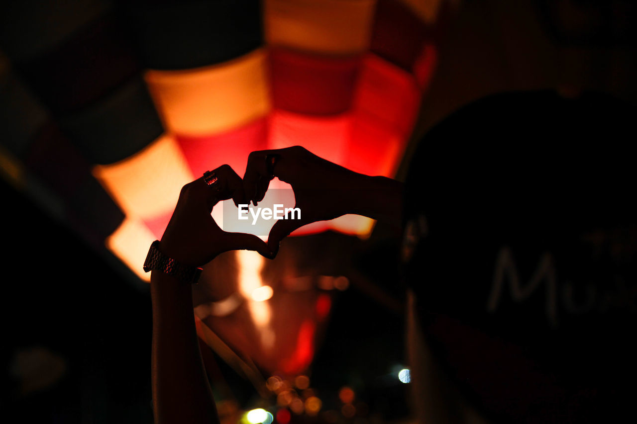 Cropped image of hands forming heart shape against hot air balloon