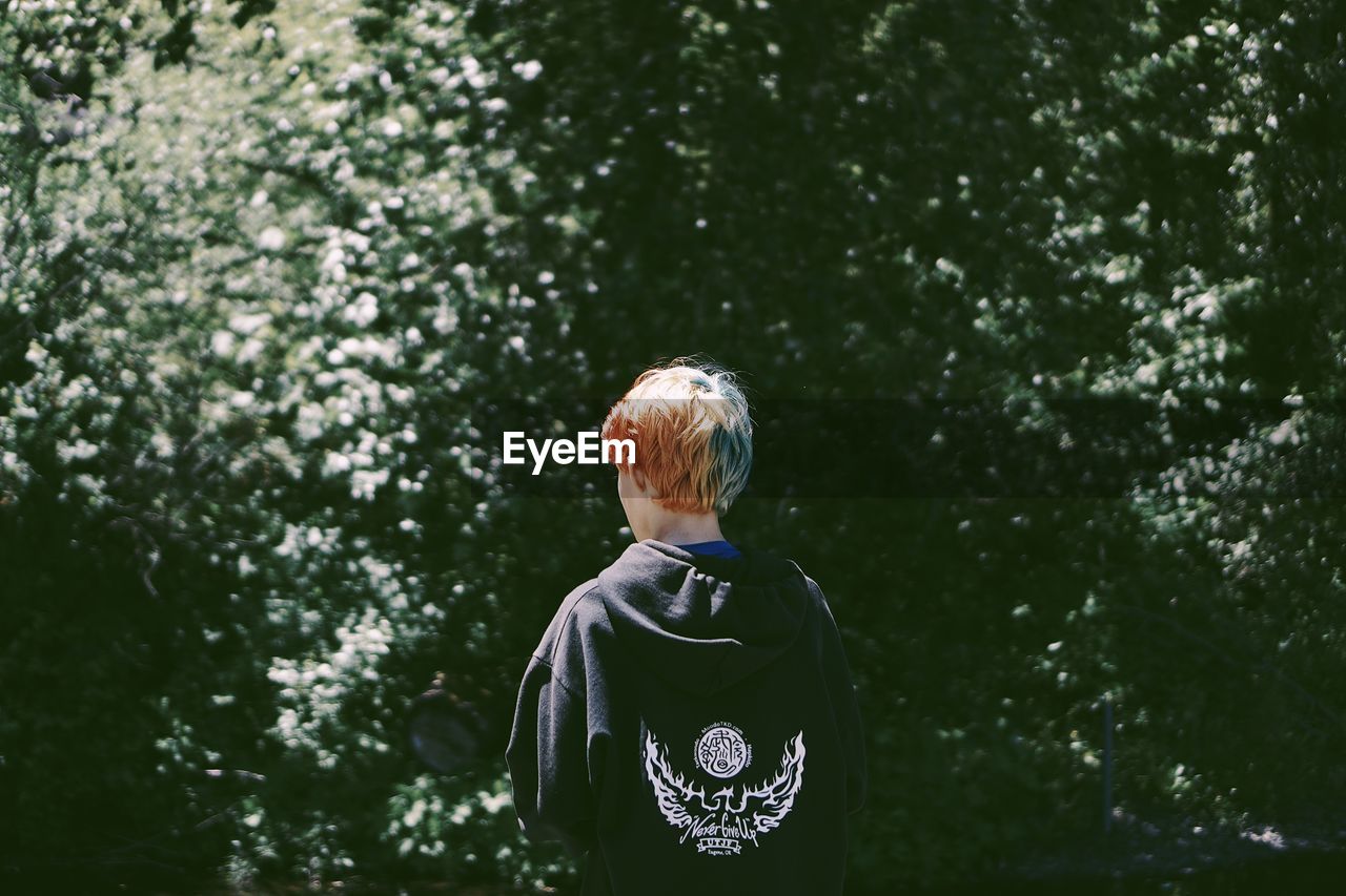 Rear view of young man standing against trees