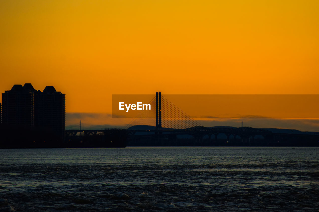 Silhouette bridge over sea against orange sky