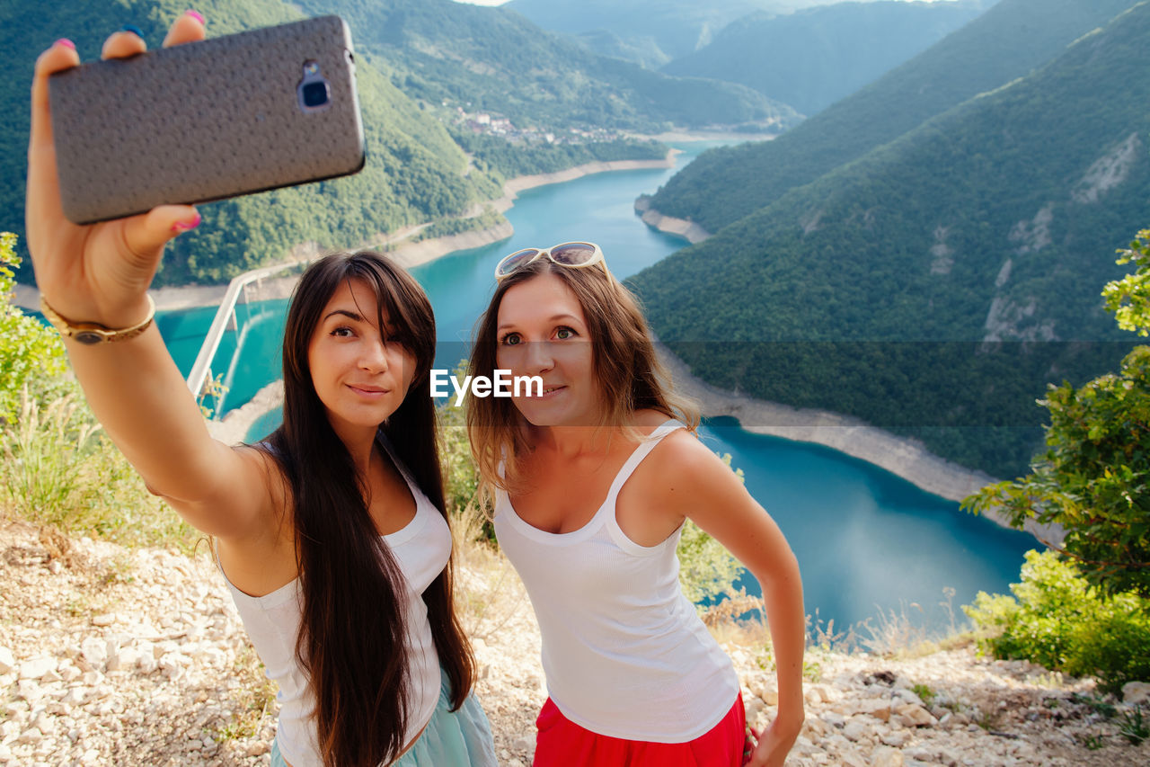 High angle view of female friends taking selfie while standing on cliff against river