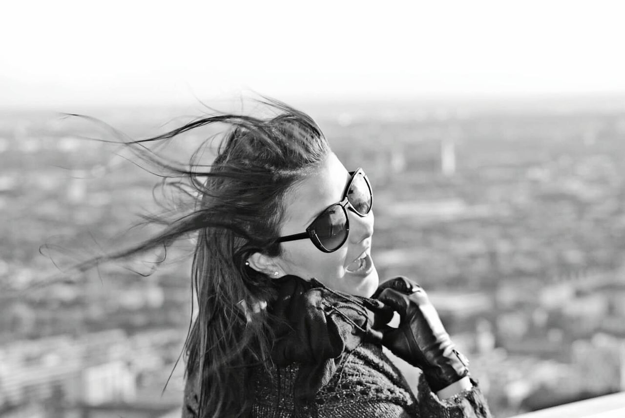 Young woman wearing sunglasses with mouth open while standing against landscape