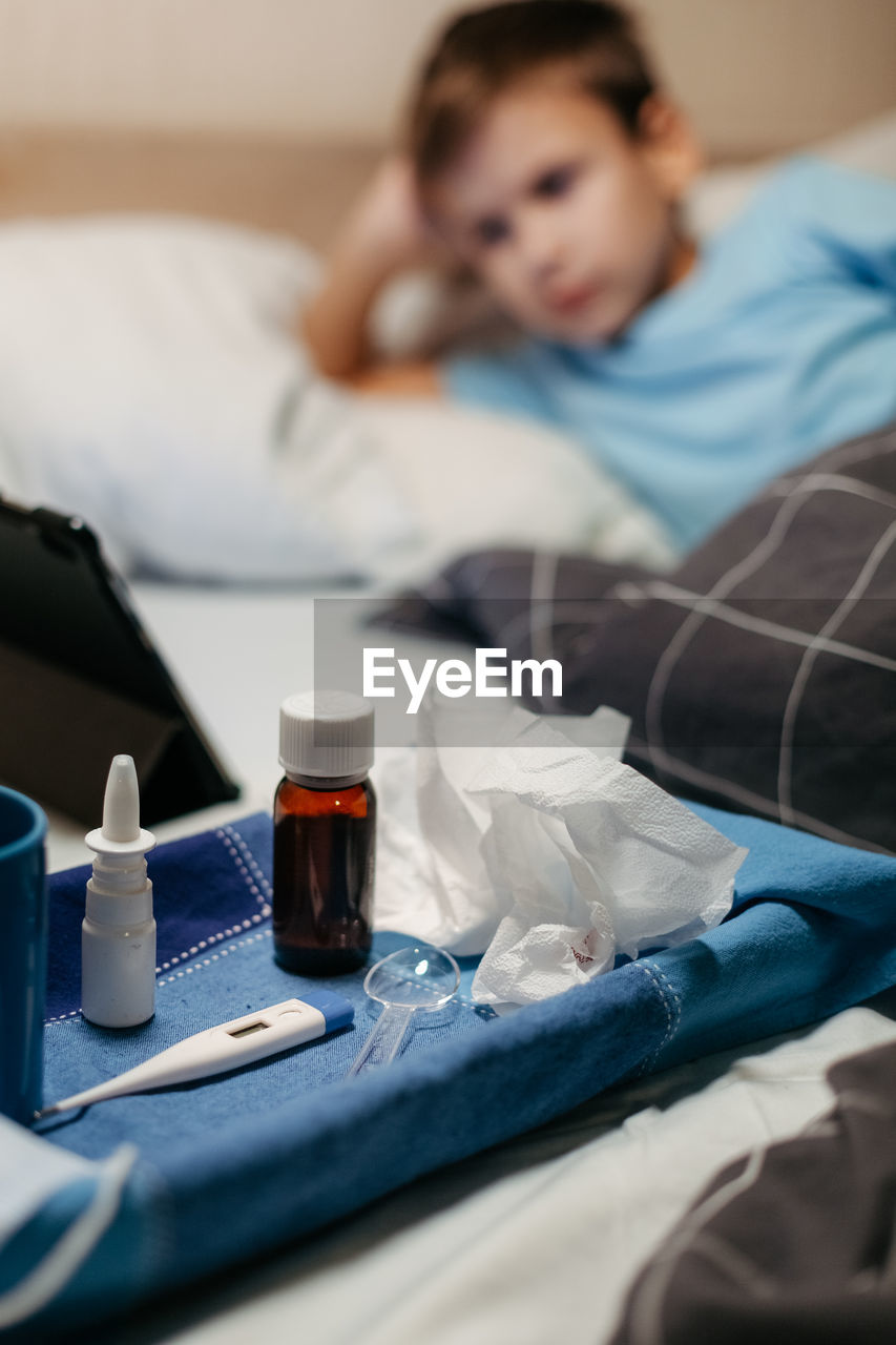Bottle with antipyretic syrup, nasal spray and thermometer on napkin. little boy on background 