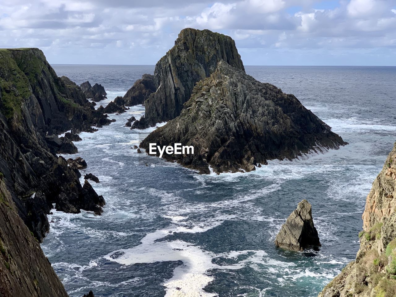 Scenic view of jagged rocks in wild sea against sky