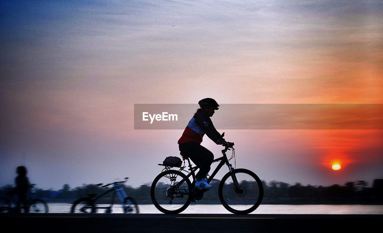 Side view of silhouette woman riding bicycle against sky during sunset