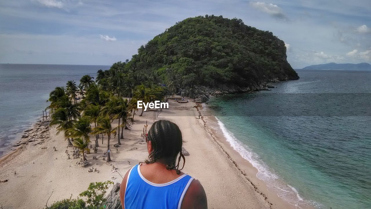 Rear view of man looking away while sitting on cliff at beach