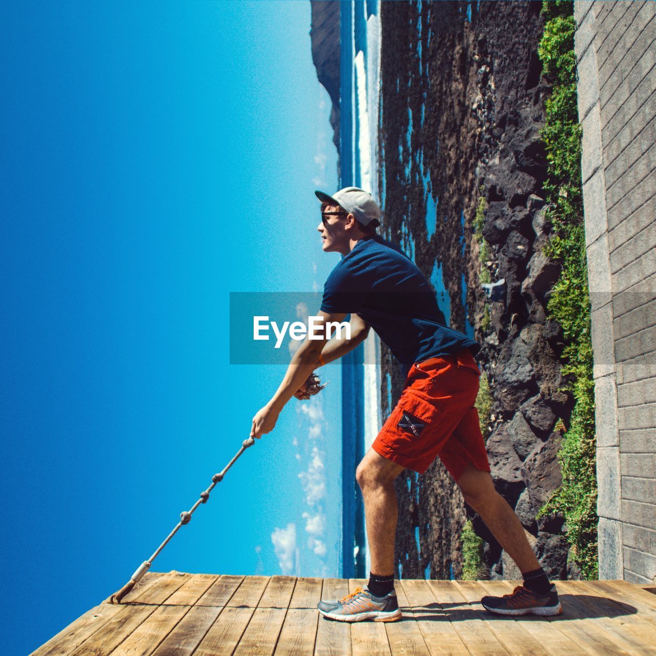 Tilt image of young man climbing wooden gate against sea