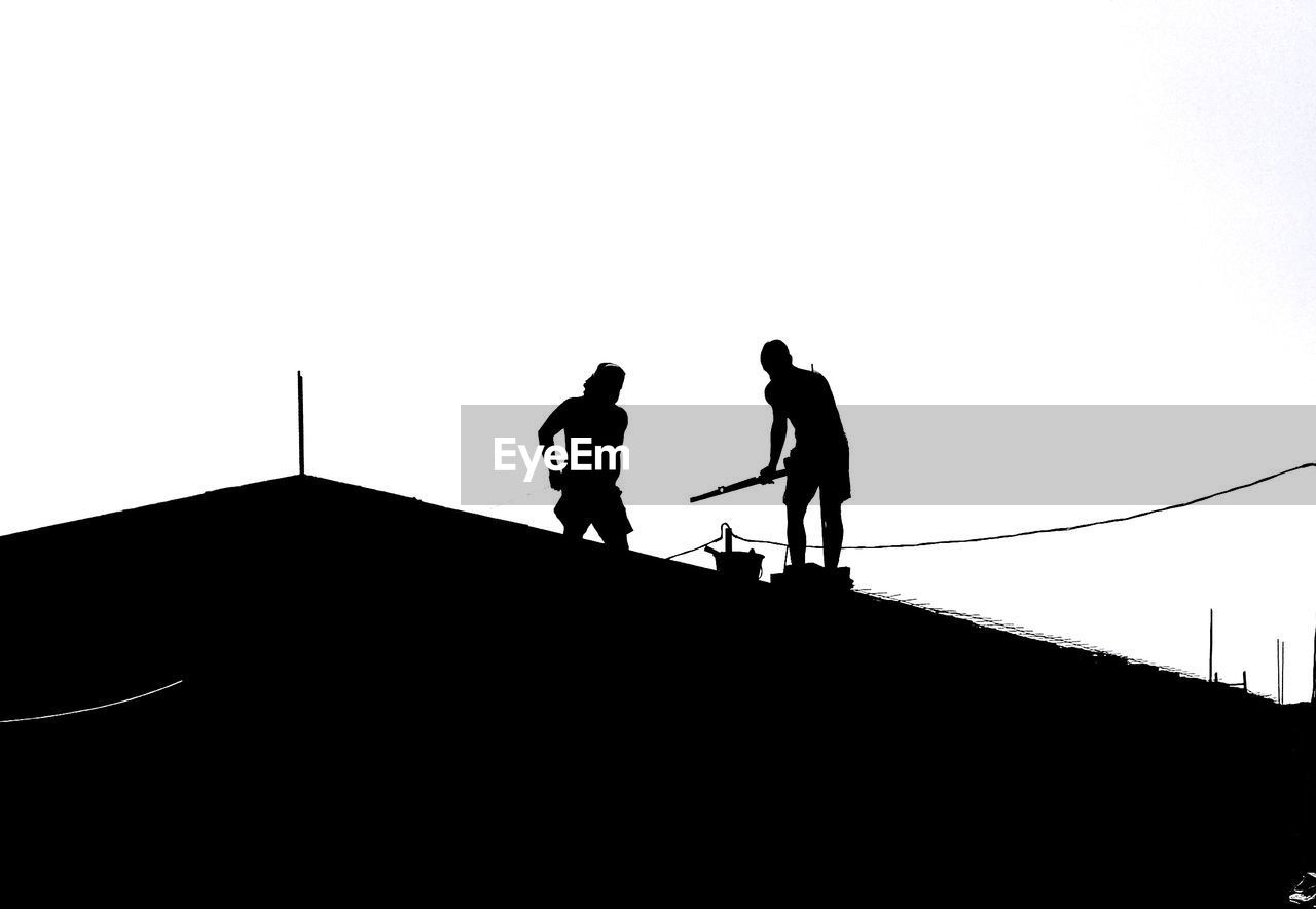 Silhouettes of men working on roof