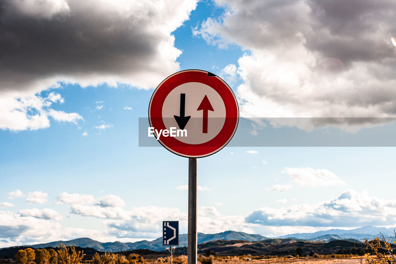 ROAD SIGN AGAINST CLOUDY SKY OVER MOUNTAIN