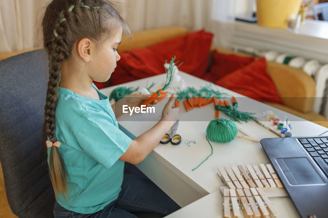 Side view of girl doing craft while watching videos on laptop at home