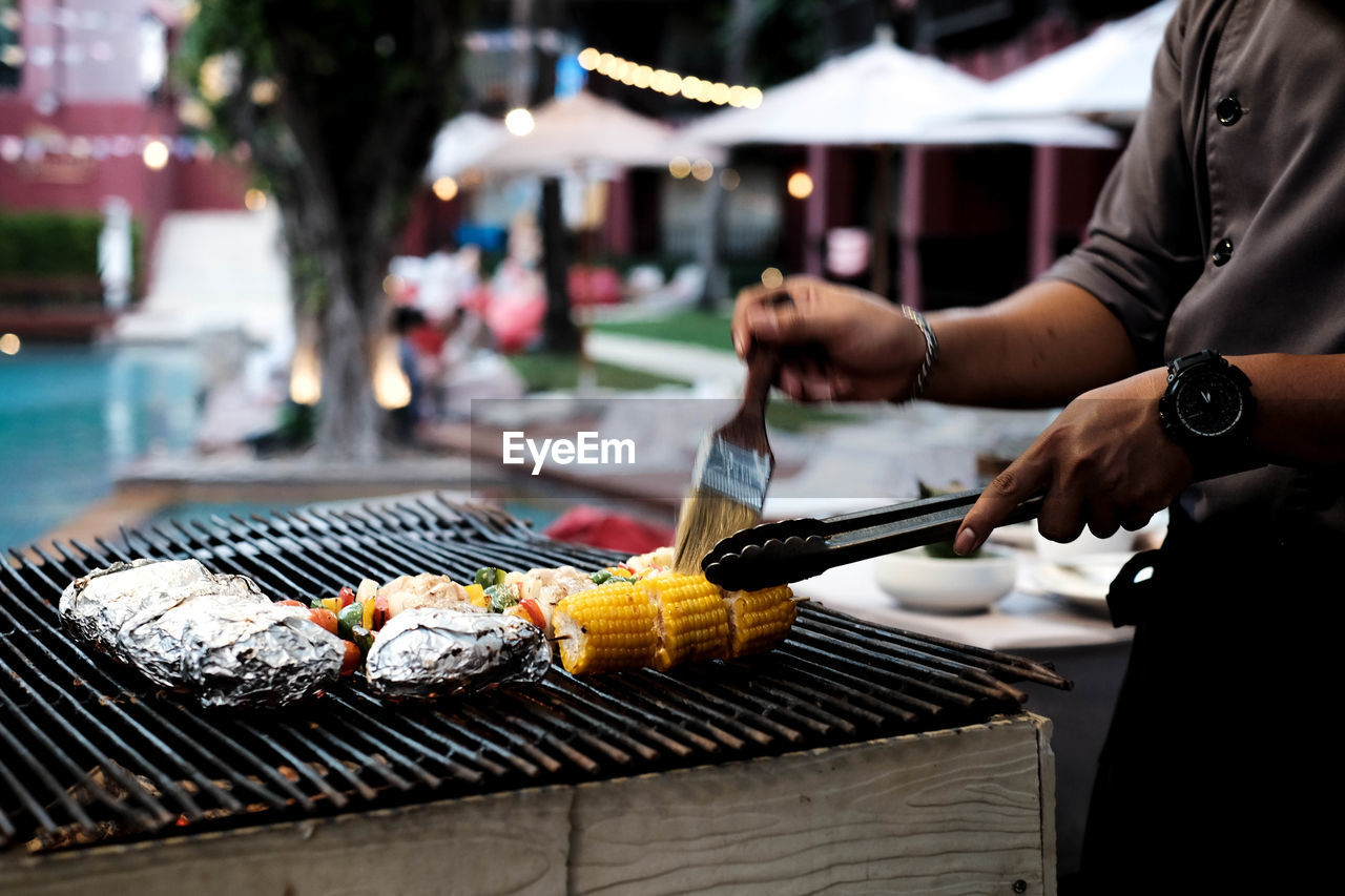 Midsection of chef barbecuing corn at pool party