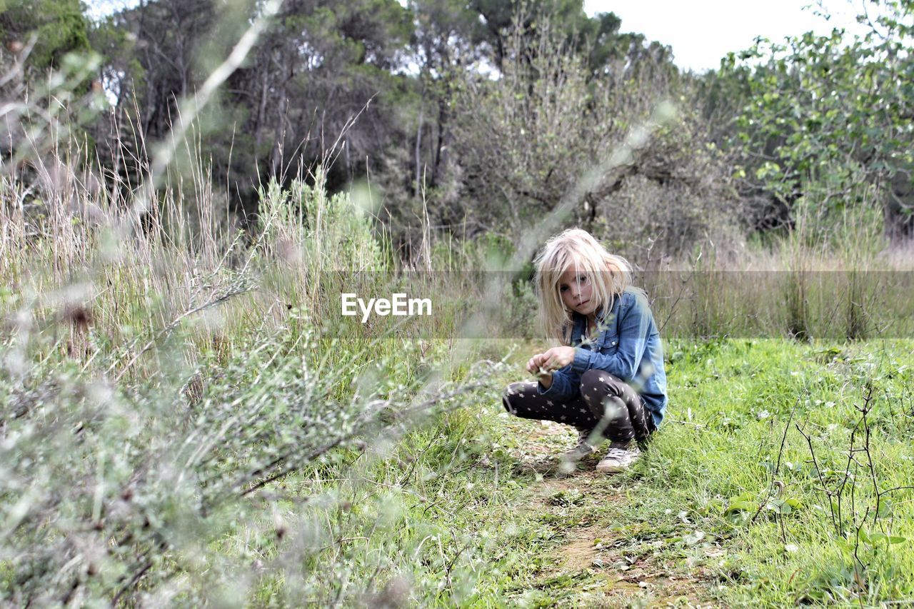 Girl crouching on grassy field against trees