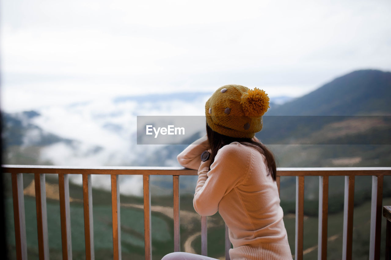 Side view of woman sitting by railing against mountains