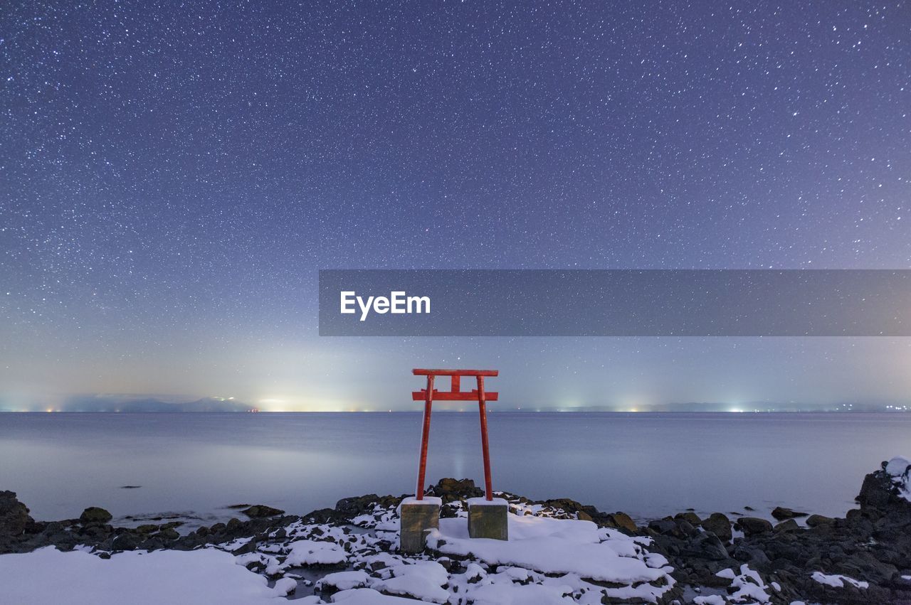 Torii gate on field against sea during winter at night
