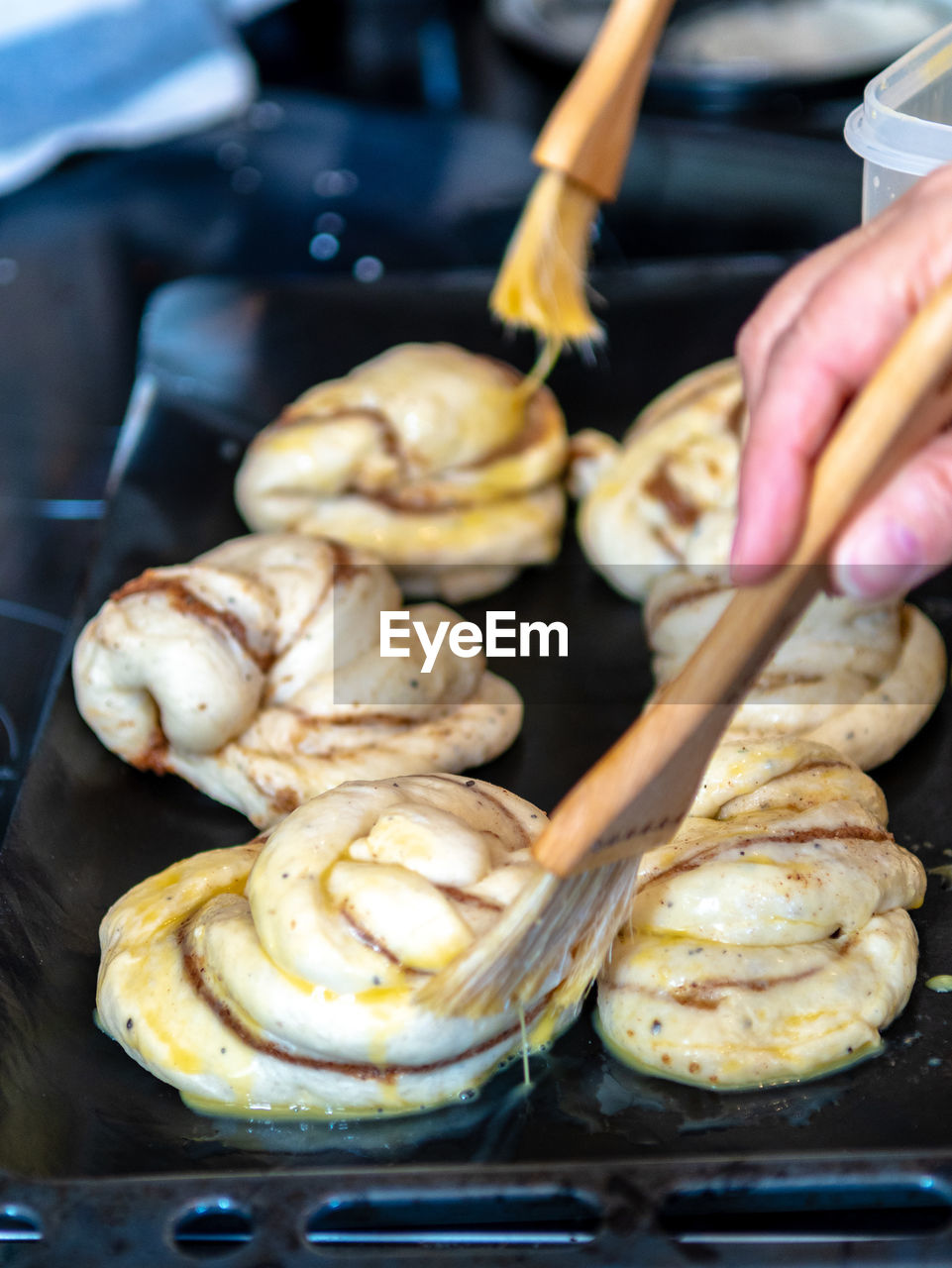Cropped hand applying egg on cinnamon rolls in backing sheet