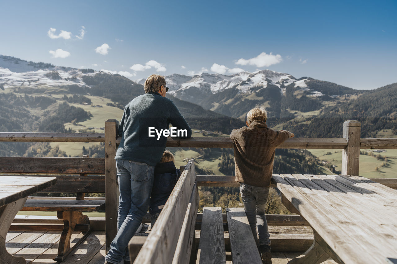 Father with two children leaning on railing while looking at leogang mountains, salzburger land, austria