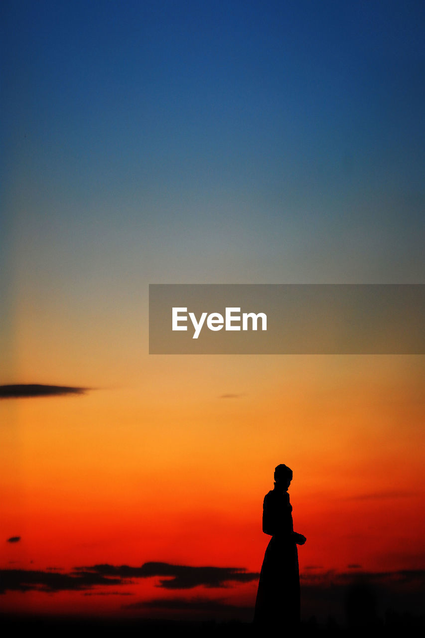 SILHOUETTE MAN STANDING AT BEACH DURING SUNSET