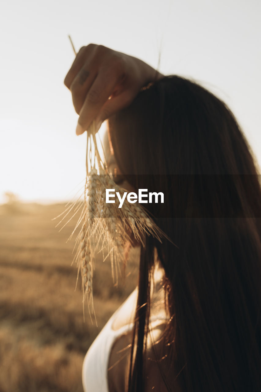 Woman holding wheat crop at farm at sunset