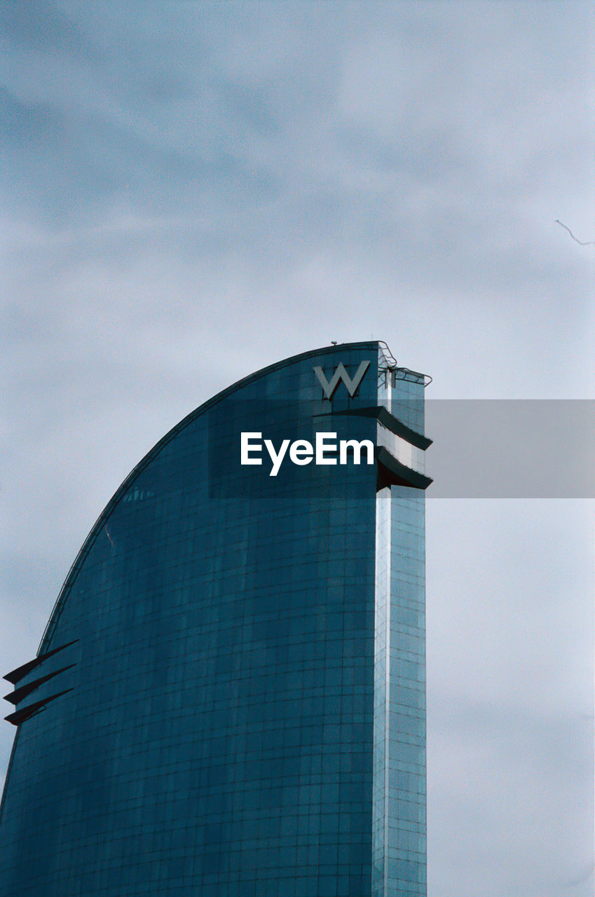 LOW ANGLE VIEW OF MODERN GLASS BUILDING AGAINST SKY