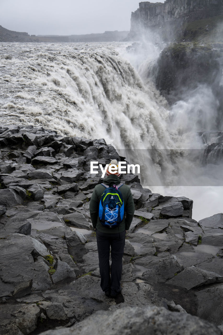 REAR VIEW OF MAN STANDING ON ROCKS