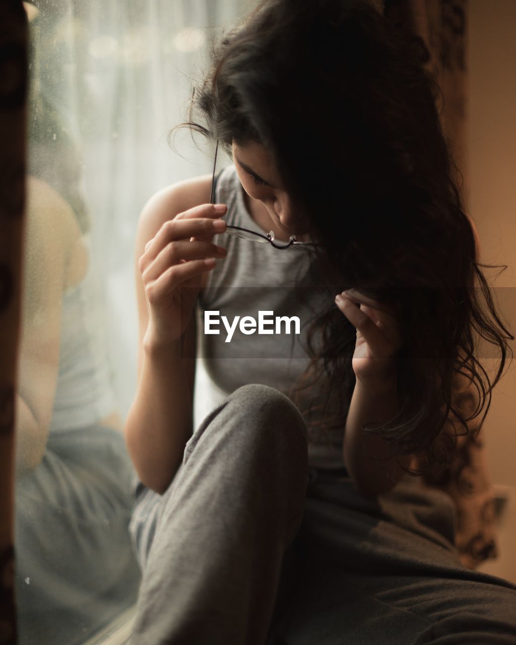 Young woman wearing eyeglasses while sitting on window sill