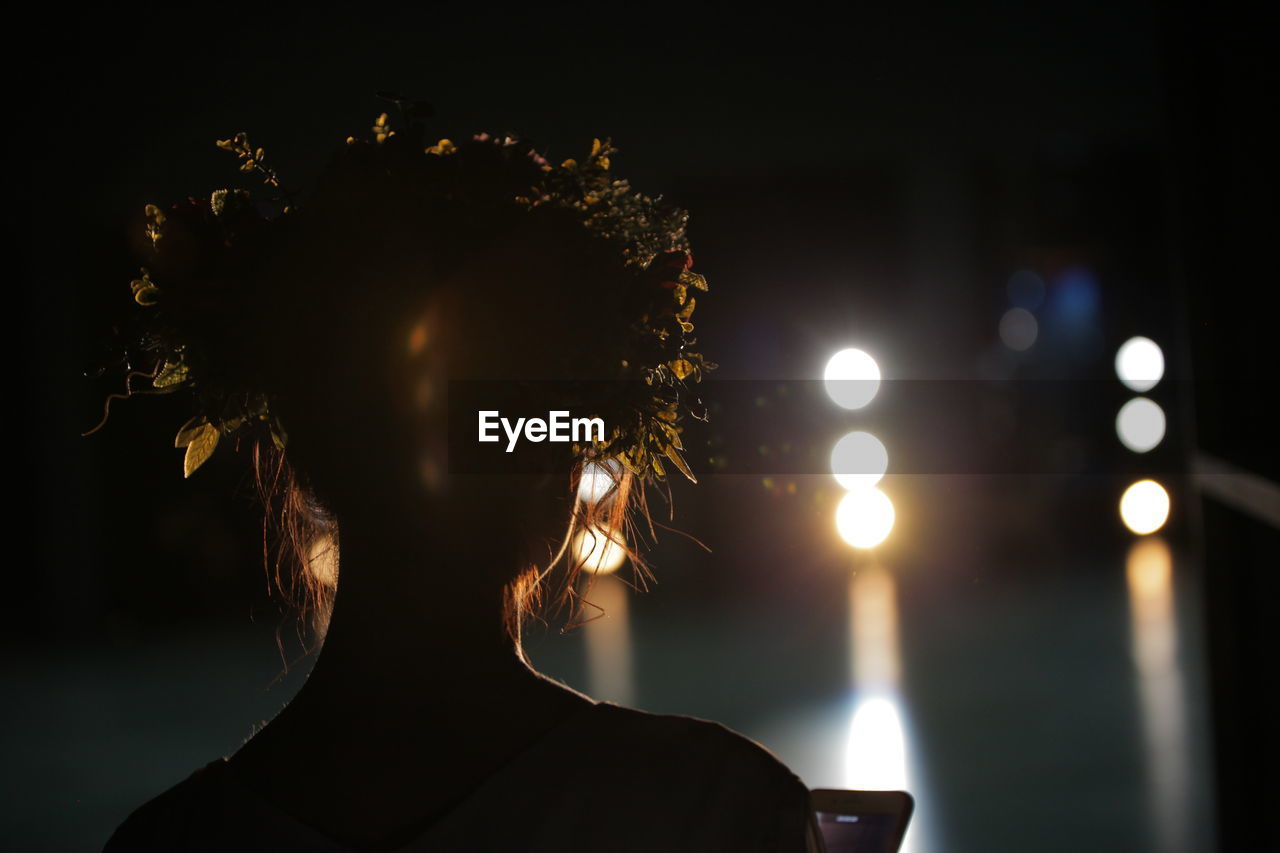 Close-up of silhouette woman against sky and illuminated lights at night