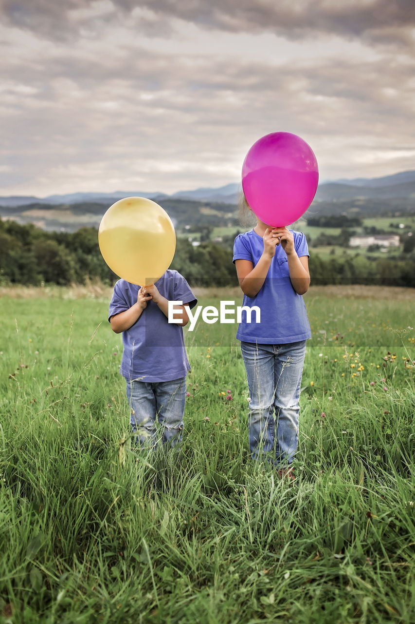 Rear view of people with balloons standing on field against sky