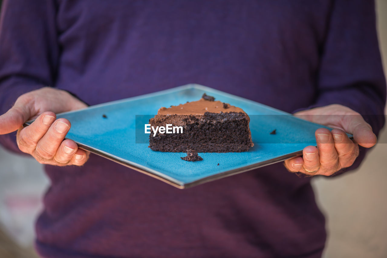 Midsection of man holding chocolate cake in plate