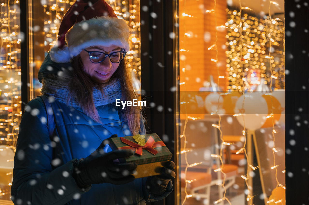 Smiling woman holding christmas gift while standing outdoors