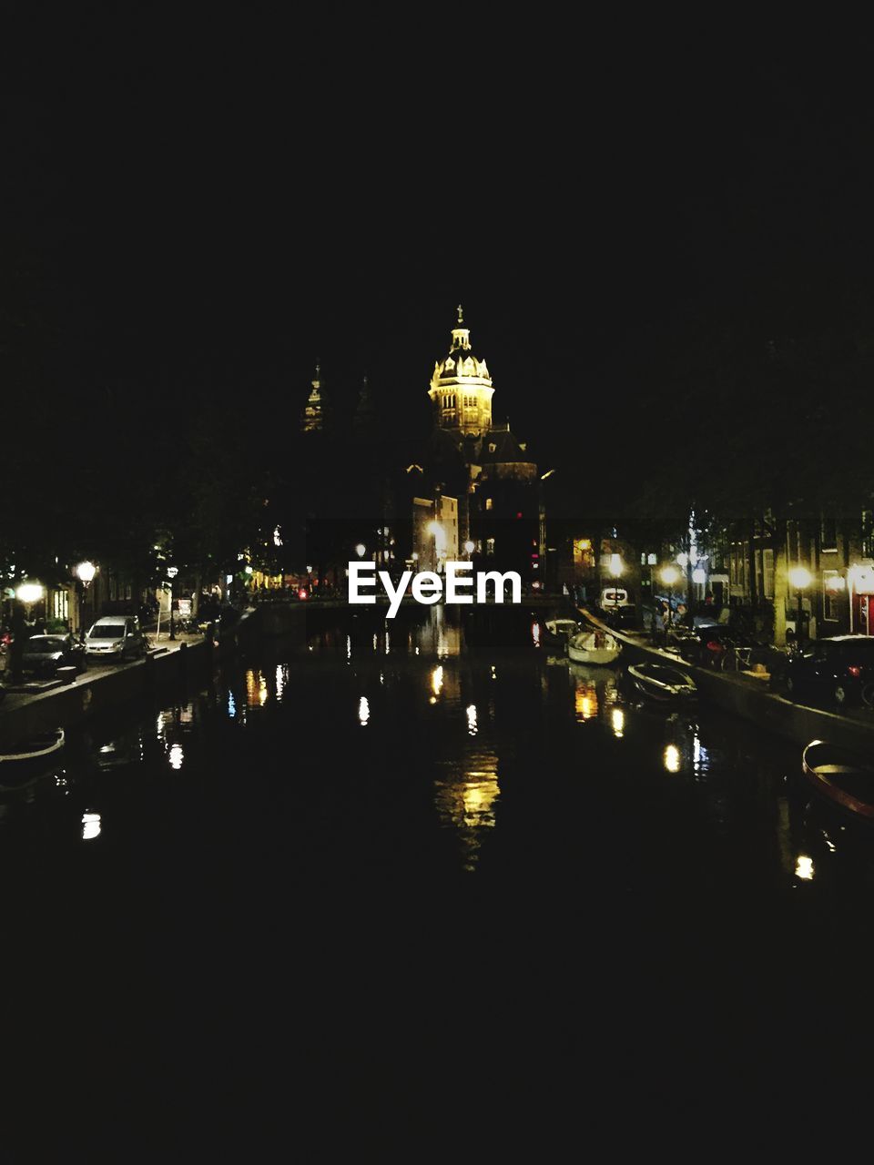 Illuminated building by canal against sky at night in city