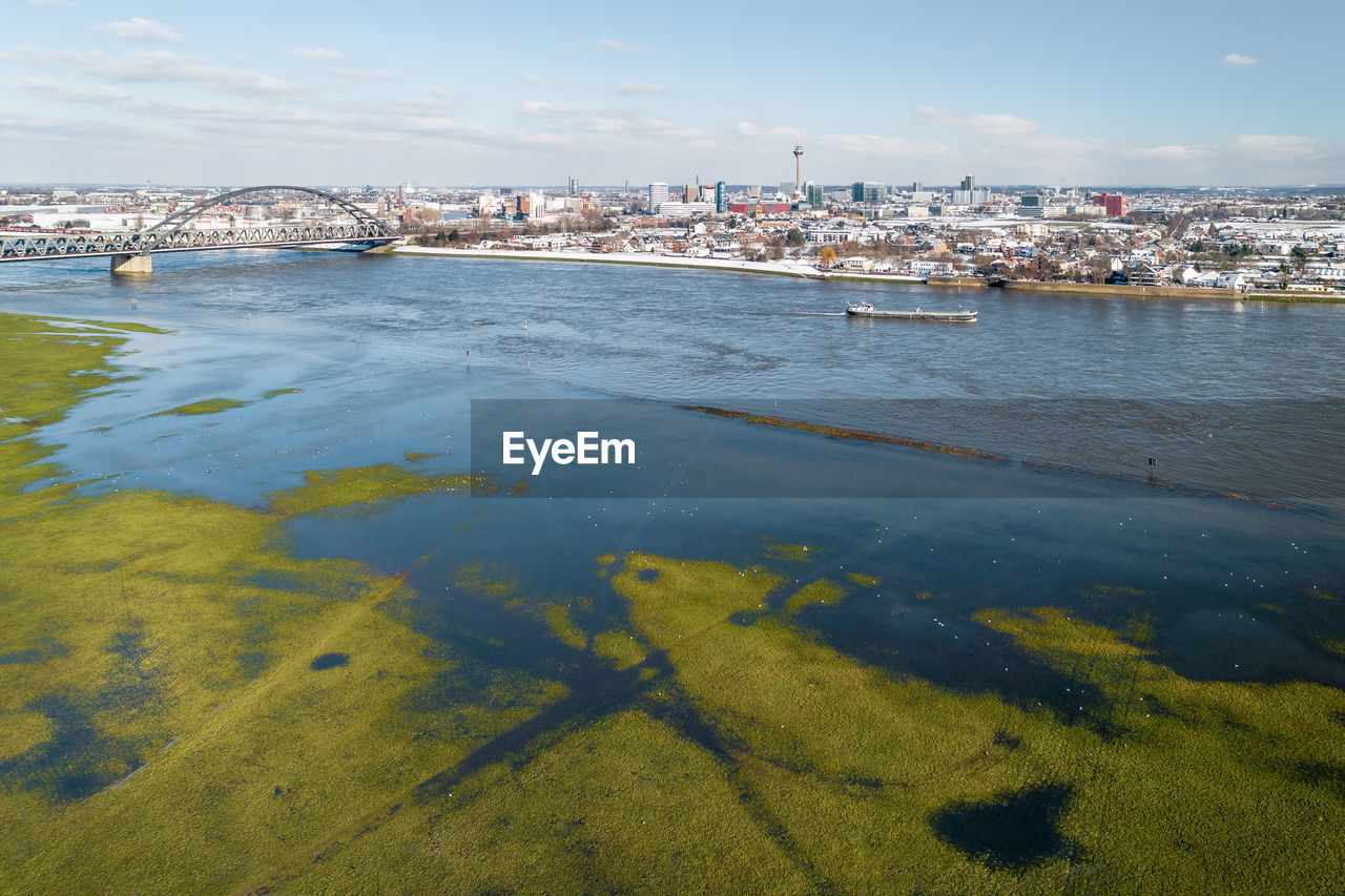 Sunlit aerial shot of flooded meadow beneath river rhine opposite to the inner city of düsseldorf