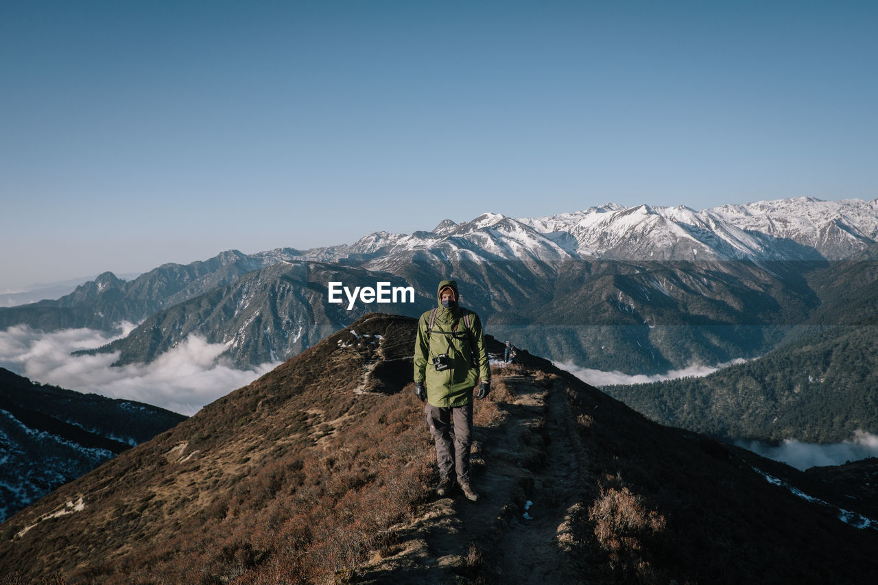 REAR VIEW OF PERSON ON SNOWCAPPED MOUNTAIN AGAINST CLEAR SKY