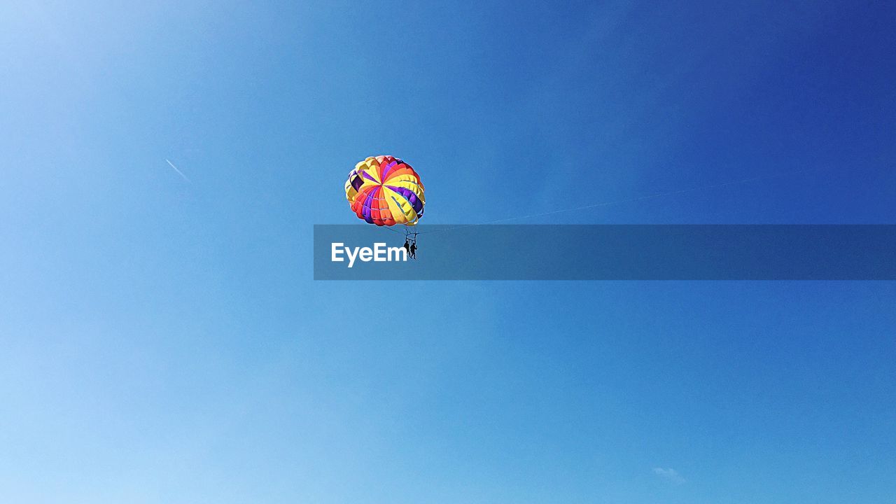 Low angle view of people paragliding against clear blue sky