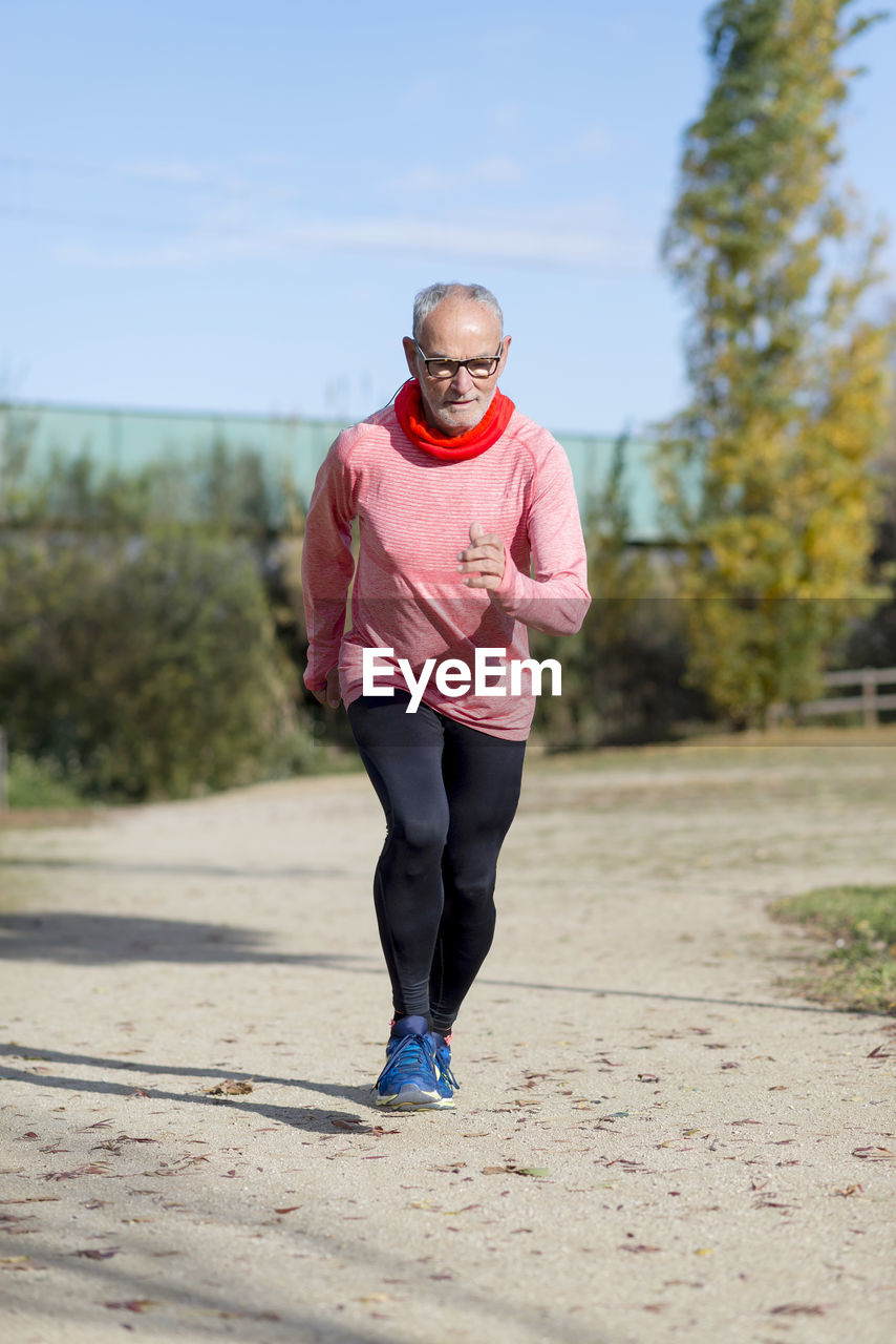 Senior man running on sand against sky