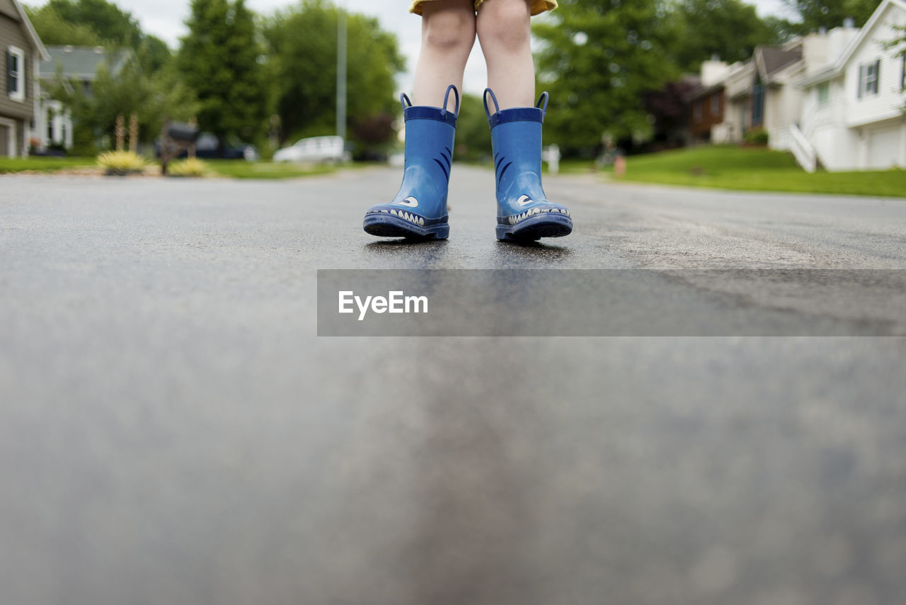 Low section of boy in rubber boots standing on wet road