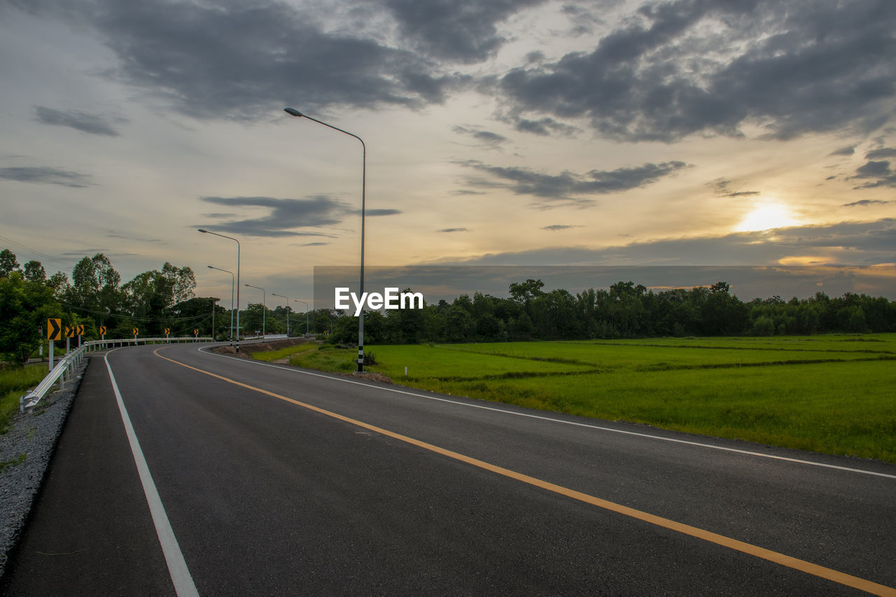 road, sky, cloud, transportation, highway, nature, plant, tree, environment, sunset, street, landscape, horizon, no people, symbol, infrastructure, sign, lane, road marking, asphalt, beauty in nature, land, marking, grass, dramatic sky, freeway, city, travel, scenics - nature, outdoors, road surface, tranquility, the way forward, moody sky, dusk, rural scene, diminishing perspective, cloudscape, street light, vanishing point, sunlight, tranquil scene, travel destinations, field