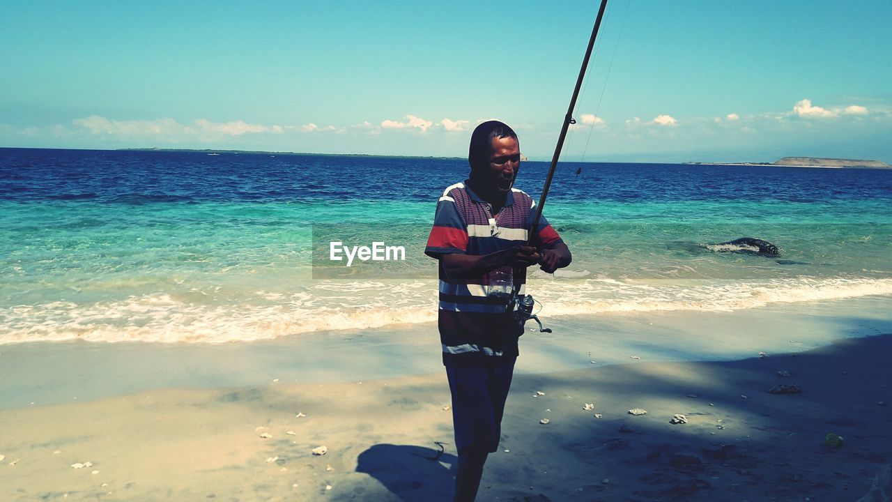 Man with fishing rod walking at beach