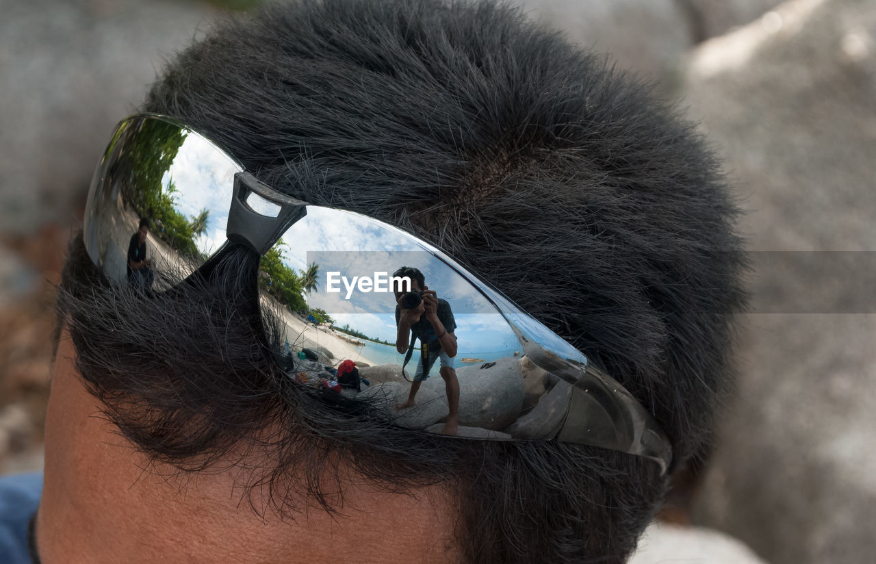 Man photographing with camera reflecting on sunglasses of man at beach