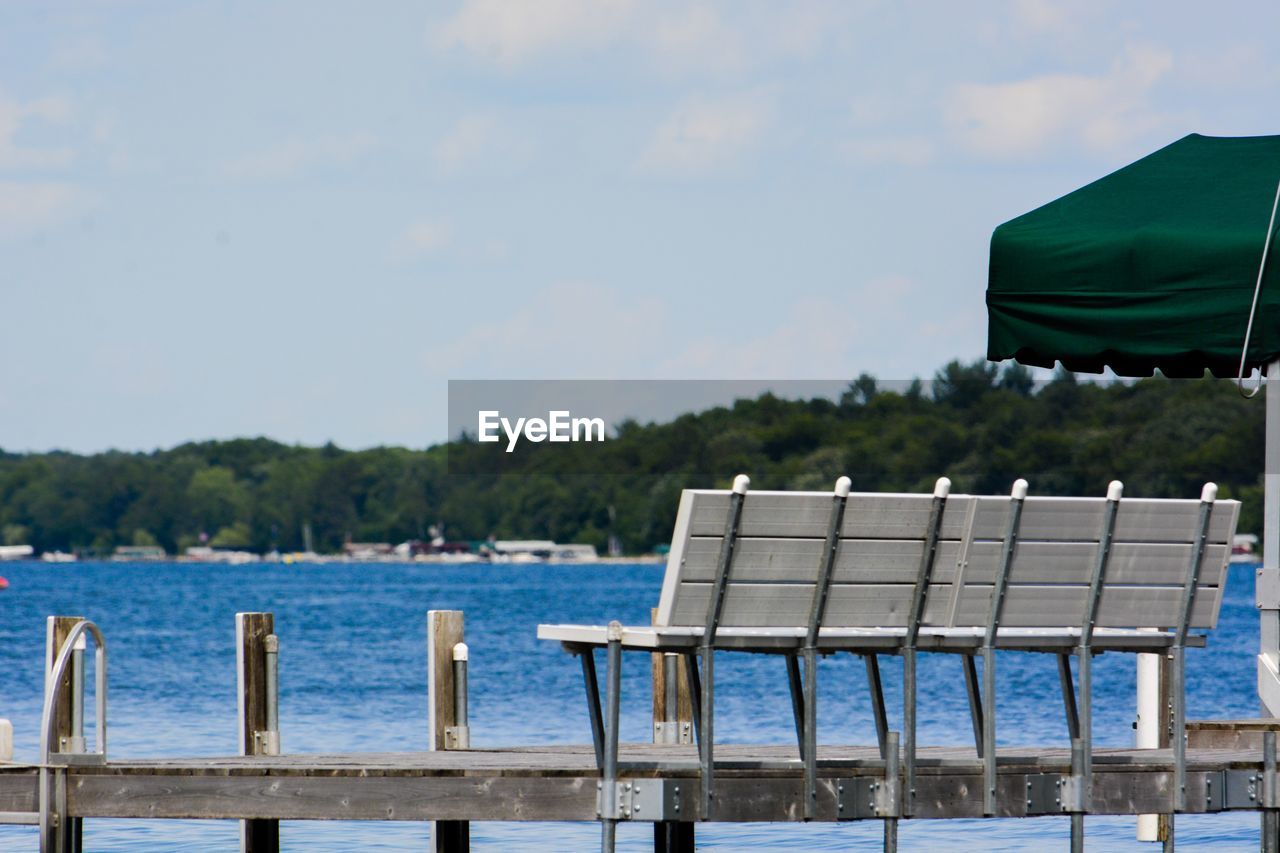 Empty bench by lake against sky