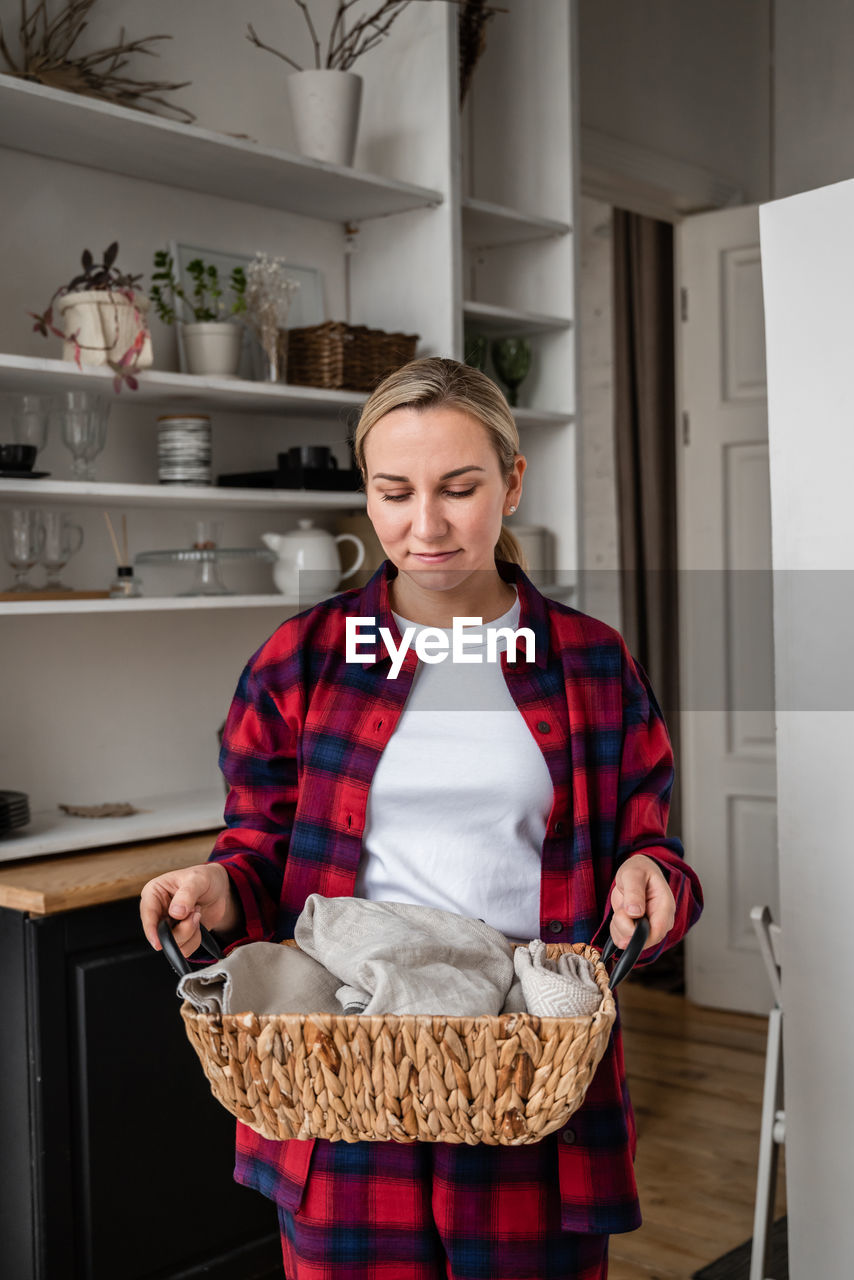 Attractive young blonde with a basket in her hands in front of her cozy kitchen. home style concept