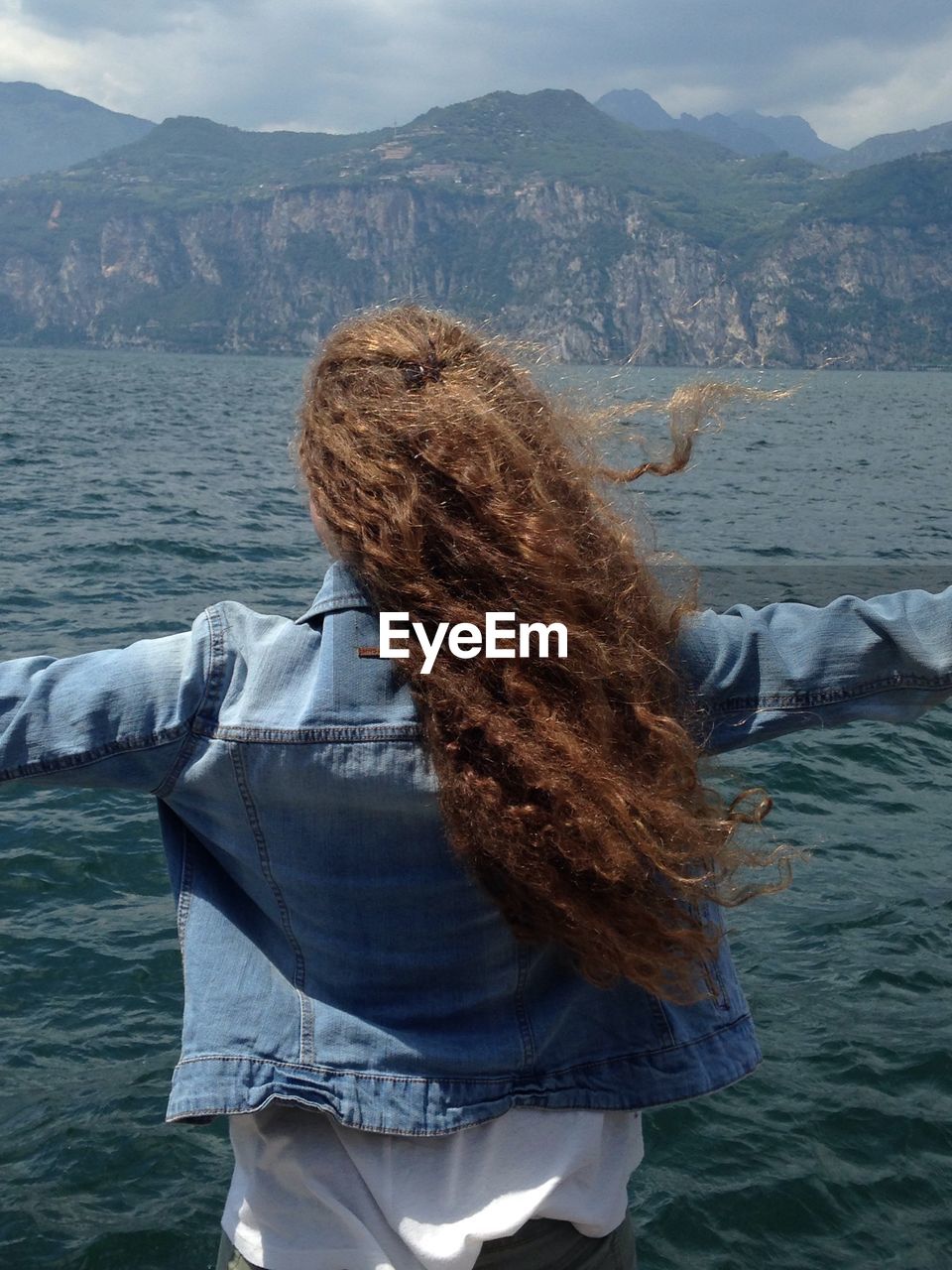 Rear view of woman with arms outstretched by lake garda