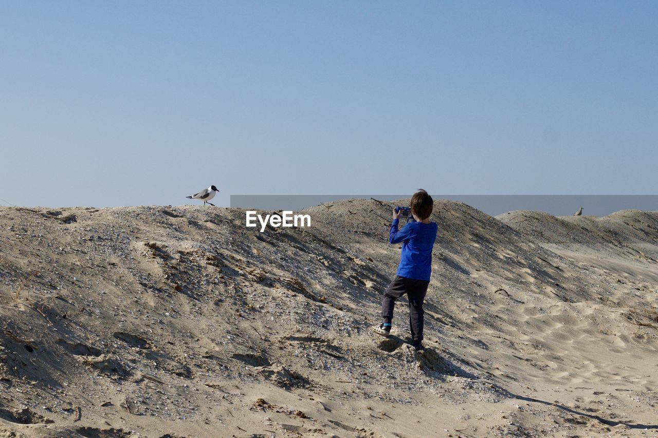 Rear view of boy standing on sand dune against sky