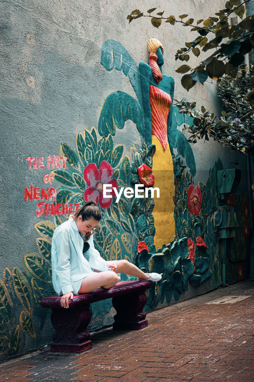 mural, art, one person, full length, creativity, painting, adult, wall - building feature, sitting, men, person, graffiti, architecture, multi colored, clothing, paint, wall, lifestyles, young adult, casual clothing, outdoors, street art, day, nature