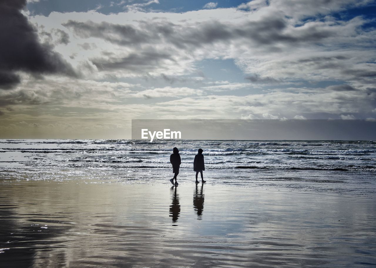 SILHOUETTE MEN ON BEACH AGAINST SKY AT SEA
